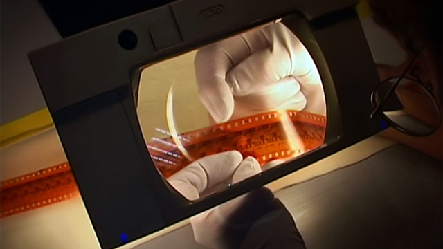 Des mains avec des gants blanc manipulent une pellicule de film